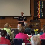 A man in uniform speaks to a group of 15 seated listeners